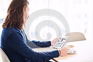 Long haired modern man with tablet sitting next to window