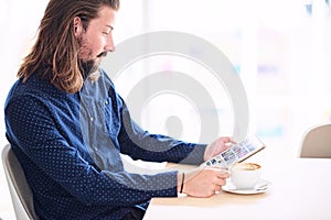 Long haired modern man with tablet sitting next to window