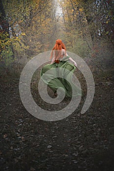 A long-haired red-haired elf girl runs away into the distance through the misty autumn forest. A fairy woman with long