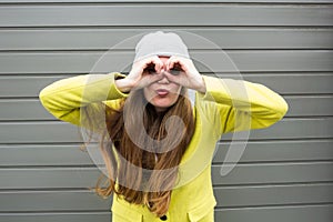 Long-haired stylish girl in a yellow coat and hat looks through binoculars. Invitation to the Journey to see the world