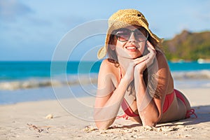 Long haired woman in bikini and straw hat lying on tropical beach