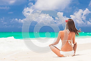 Long haired woman with flower in hair in bikini at tropical beach