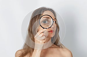 Long-haired woman with magnifying glass looking at camera with big zoom eye, checking authenticity. Verification, choice concept photo