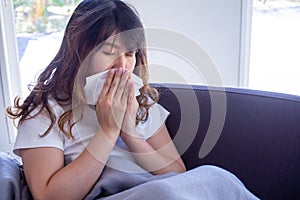 Long haired woman sitting on the sofa is suffering from flu, cough and sneezing. Sitting in a blanket because of high fever and