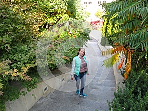 Long-haired young adult girl in autumn clothes walks up the stairs, top view