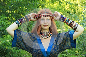 Long-haired young Caucasian girl with red hair in a traditional dress adorned with many African necklaces