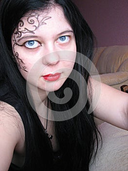 Long-haired young Caucasian gothic girl with black hair, in black clothes, with a cross on her neck