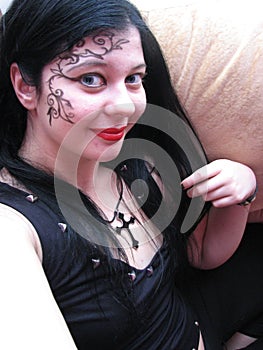 Long-haired young Caucasian gothic girl with black hair, in black clothes, with a cross on her neck