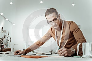 Long-haired young designer from a fashion school in a brown garment making notes