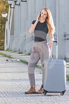 Long haired  young girl is phoning standing next to the suitcase