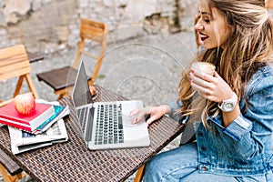 Long-haired young smiling woman drinks milk shake working with the laptop. Pretty female freelancer checks the mail
