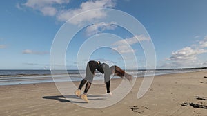 Long-haired young woman practices front and back handspring and cartwheel on beach with sea view. Slow motion