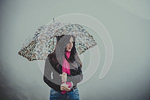 Long-haired young woman stands under an umbrella and outside it rains, the background is a white cloud