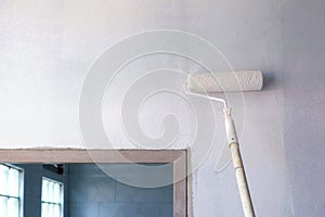 Long handle roller brush applying white primer paint on concrete wall photo
