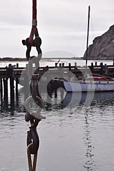 Long hanging metal chain link with an old boat docked at the pier with Morro Rock in the distance