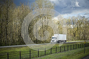 Long haul industrial big rig semi truck with dry van semi trailer transporting goods running on the divided highway road with bare