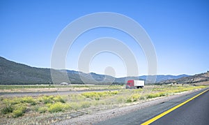 Long haul industrial freight big rig red semi truck with semi trailer transporting goods driving on the flat road in California