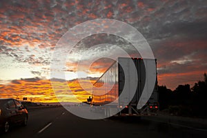 Long haul truck driving on a desert highway at sunrise or sunset