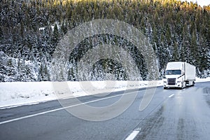 Long haul white big rig semi-truck transporting cargo in dry van semi-trailer climbing uphill on the winter slippery iced highway