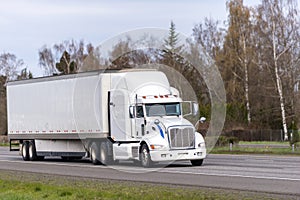 Long haul white big rig semi truck transporting goods in dry van semi trailer running on straight highway road