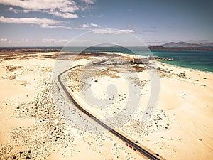 Long highway asphalt road with desert and sand beach on both sides - aerial high view with ocean and islands on background -