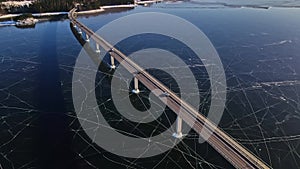 Long highway bridge over a frozen river with clear cracked ice and traffic driving by.