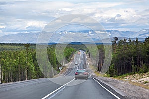 Long highway stretches away to mountains on horizon. Cars driving on asphalt road the Kola. It is way to the Murmansk city on