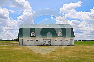 A long horizon view of a bright white farm barn with green trim and green tin rood in a grass field
