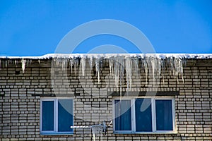 Long icicles and snow hang on the eaves of the house roof