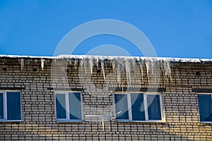 Long icicles and snow hang on the eaves of the house roof