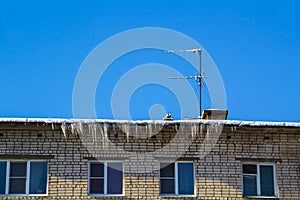 Long icicles and snow hang on the eaves of the house roof