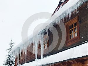 Long icicles on a traditional wooden building. House in mountain town in winter. Windows, snow, ice. Zakopane, Poland, Tatra mount