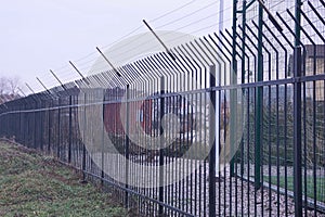 Long iron green fence of twigs and barbed wire on the street