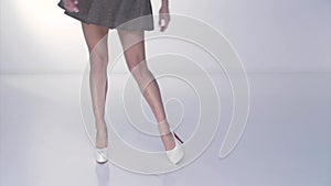 Long legs of young beautiful woman on white high heel, a red sole of shoes, a short skirt, feet go on a white background