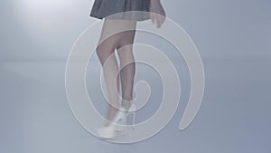 Long legs of young beautiful woman on white high heel, a red sole of shoes, a short skirt, feet go on a white background