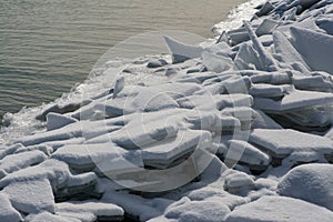 Long line of rocks along Lake Michigan shoreline covered with frozen ice and snow on a sunny winter