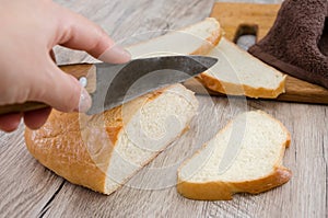 Long loaf on a wooden board and knife. Delicious Ukrainian bread. Hand cuts a knife with white bread, close-up ..