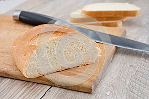 Long loaf on a wooden board and knife. Delicious Ukrainian bread. Sliced white bread.