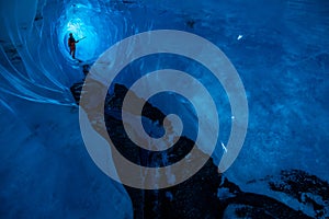 Long narrow ice cave in a glacier in remote Alaska. Man stands in the back under a thin section of ice with light shining through