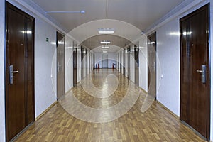 Long office hallway with many doors of dark red wood.