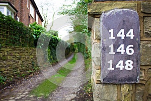 Long Overgrown Pathway With Slate Numbers On A Wall