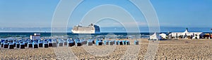Long panorama of the Baltic Sea beach with deck chairs and a large cruise ship