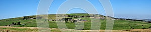 Long panoramic view of green fields and village stone houses in rolling west yorkshire dales countryside in colden with blue