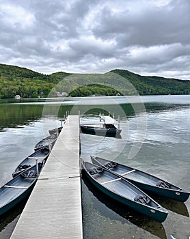 long pier with boats on lake (dock for canoes and kayaks with mountain view and dark cloudy sky) rowing