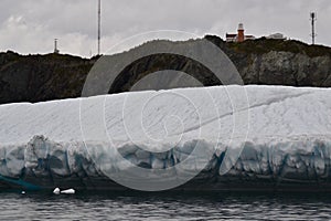 Long Point Lighthouse at the top of cliff in Twillingate Harbour with large iceberg in foreground