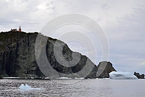 Long Point Lighthouse at the top of cliff in Twillingate Harbour with large iceberg stranded nearby