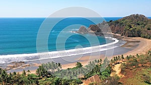 Long pull back aerial reveal over idyllic palm tree tropics, Costa Rica sandy beach and ocean waves