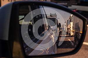 Long queue of trucks and cars as part of a traffic jam on a motorway in italy, europe on a sunny day.  Looking through rear view
