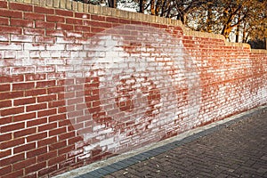 A long red brick wall stained with white efflorescence, a crystalline of salt, formed due to water being present