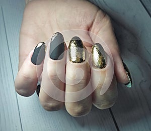 Long round nails with black matte gel polish and gold design. Manicure on women`s hands with gel coating.